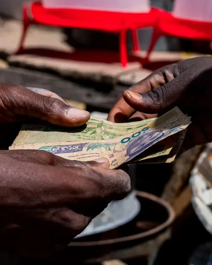 Deux mains qui se passent des billets au-dessus d’une planche de comptoir, sur un marché.